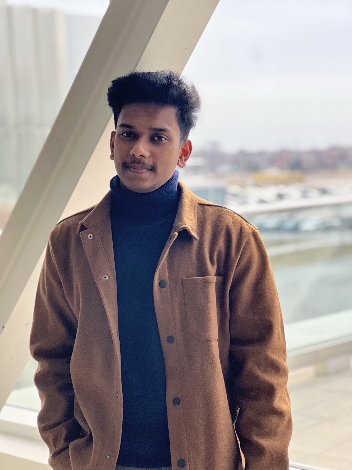 Sonu wearing a warm brown jacket beside a window